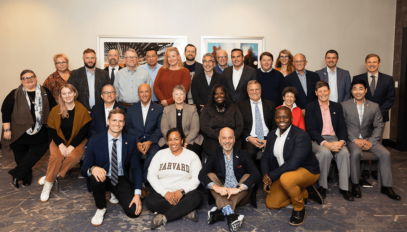 A couple dozen individuals in business attire pose in three rows for the camera and smile.