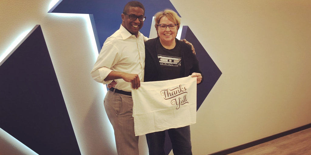 Reggie Greer and Nancy Van Reece pose in front of the Victory logo with a "Thanks y'all" sign