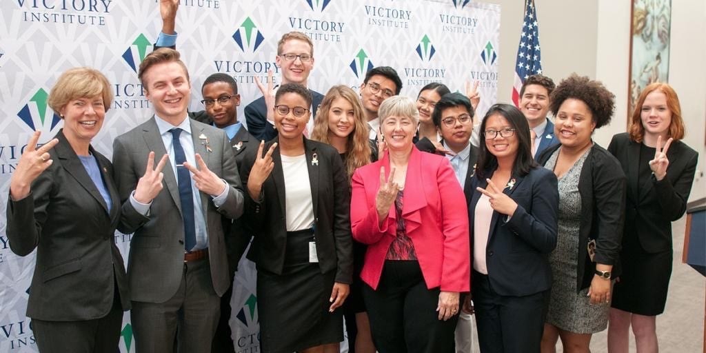 The 12 Victory Congressional Interns pose with Senator Tammy Baldwin and Mayor Annise Parker all making peace signs for the camera 