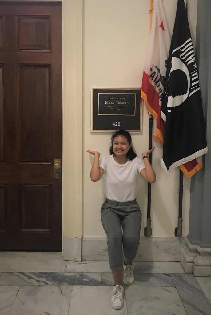 A Victory Congressional Intern poses underneath the sign for Representative Mark Takano's Office